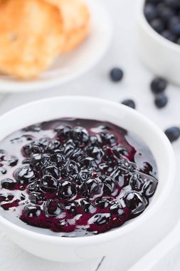 Fresh homemade jam made of Patagonian Calafate berries (lat. Berberis heterophylla), served in white bowl, toasted bread and raw berries in the back (Selective Focus, Focus one third into the image)