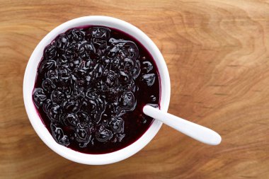 Fresh homemade jam made of Patagonian Calafate berries (lat. Berberis heterophylla) served in white bowl, photographed overhead on wood (Selective Focus, Focus on the jam)