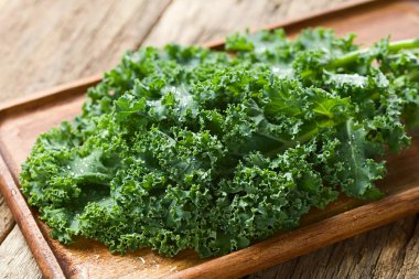 Fresh raw curly kale or leaf cabbage (lat. Brassica oleracea) photographed on wooden board (Selective Focus)