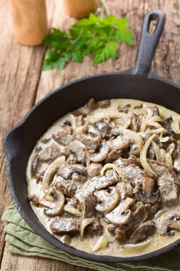 Fresh homemade creamy beef stroganoff with mushroom slices and onion in cast-iron skillet (Selective Focus, Focus one third into the pan)