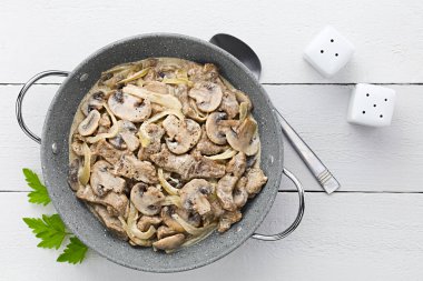 Fresh homemade creamy beef stroganoff with mushroom slices and onion served in bowl, photographed overhead on white wood (Selective Focus, Focus on the dish)
