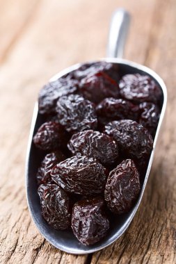 Dried plums on metal scoop on wood (Selective Focus, Focus one third into the image) clipart