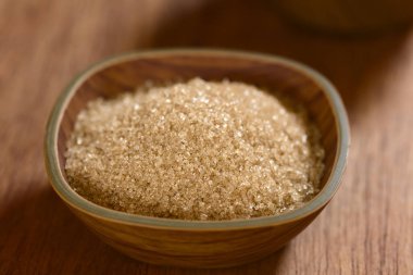 Kahverengi şeker kristalleri küçük kasede, ahşap tahtada doğal ışık ile fotoğraflanmış (Çok Sığ Alan Derinliği, kasenin üçte birine odaklanın)