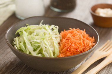 Rendelenmiş havuçtan yapılmış lahana salatası ve kasede doğranmış beyaz lahana, arkada mayonez, tuz ve biber ile hazırlanıyor (Seçici Odak, kasenin üçte birine odaklan)