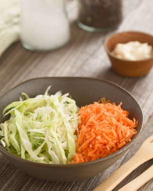 Rendelenmiş havuçtan yapılmış lahana salatası ve kasede doğranmış beyaz lahana, arkada mayonez, tuz ve karabiber ile hazırlanıyor (Seçici Odak, görüntünün üçte birine odaklan)