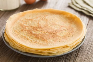 Bir yığın taze ev yapımı krep, ince Fransız usulü krep, arkasında un ve yumurta olan tabakta (Seçici Odaklanma, üçte birini kreplere odakla)