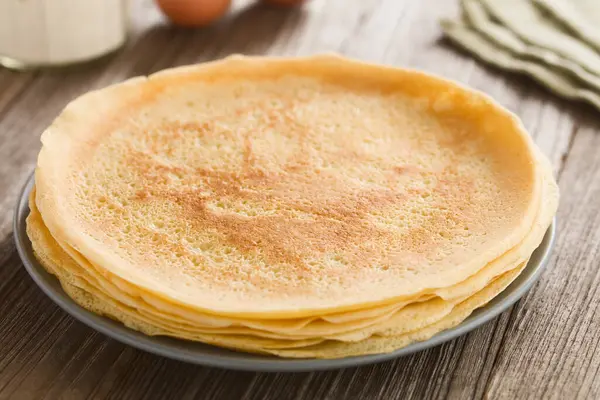 Bir yığın taze ev yapımı krep, ince Fransız usulü krep, arkasında un ve yumurta olan tabakta (Seçici Odaklanma, üçte birini kreplere odakla)