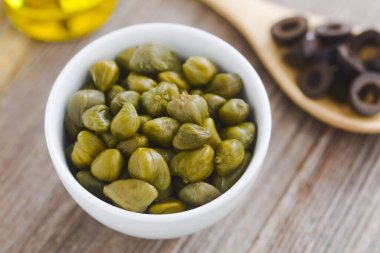 Arkasında siyah zeytin dilimleri ve zeytin yağı bulunan küçük kasede turşulu kapari, Fransız tapenatasının malzemeleri yayıldı (Seçici Odaklanma, kaparilerin üçte birine odaklan)  