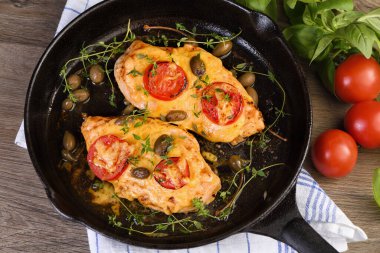 Tender chicken breast baked with tomatoes, capers, herbs under cheese crust in a frying pan