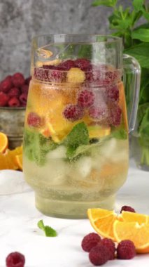 Yaz Sangria kokteyli ya da ahududu, portakal ve naneli limonata. Ferahlatıcı, alkolsüz, detoks, sağlıklı içecek, cam sürahide meyve. Dikey video, kamera ileri gidiyor.