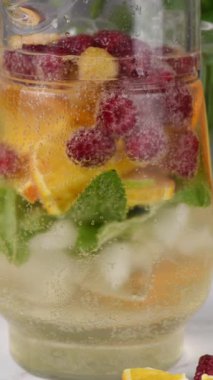 Yaz Sangria kokteyli ya da ahududu, portakal ve naneli limonata. Ferahlatıcı, alkolsüz, detoks, sağlıklı içecek, cam sürahide meyve. Dikey Video, Makro.