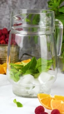 Yaz Sangria kokteyli ya da ahududu, portakal ve naneli limonata. Ferahlatıcı, alkolsüz, detoks, sağlıklı içecek, cam sürahide meyve. Dikey video, kamera ileri gidiyor.