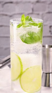 Naneli Mojito bardağın içinde fokurduyor, yavaş çekimde farklı yönlere savruluyor. Cama bir kokteyl tüpü yerleştiriliyor. Yakın plan. Bu bir dizi dikey videonun bir parçasıdır..