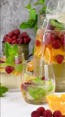 Meyve bardağını Summer Sangria kokteyliyle ya da ahududu, portakal ve nane ile doldurmak. Organik alkolsüz, detoks, sağlıklı içecek kamera ileri, yavaş çekim. Dikey video 