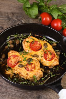 Tender chicken breast baked with tomatoes, capers, herbs under cheese crust in a frying pan