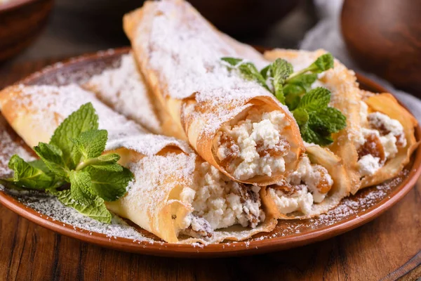 stock image Thin pancakes filled with cottage cheese, honey and raisins, rolled in the form of a tube, sprinkled with powdered sugar, garnished with mint. Festive dish for the pagan Slavic holiday Maslenitsa