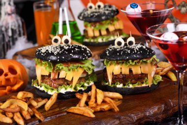 Canavar Burger. Siyah çörek, sulu sığır pirzolası, marul, soğan, diş şeklinde domates ve peynir, zeytinli mozarella gözler. Kesinlikle canlandırıcı ve mükemmel bir Cadılar Bayramı partisi aperatifi..