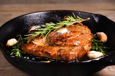 Pork cutlet on the bone in a piece of butter with garlic and rosemary in a frying pan  clipart