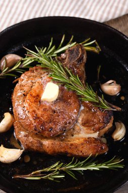 Kemiğin üzerinde domuz pirzolası bir parça tereyağında sarımsak ve biberiyeyle kızartma tavasında. 