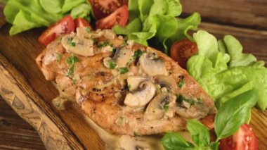 Mantar soslu tavuk göğsü ve ahşap tabakta sebzeler. Yavaş çekim videosu, soldan sağa dairesel hareket. Yakın plan.