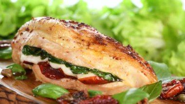Ispanak, kurutulmuş domates ve mozzarella ile doldurulmuş çıtır çıtır tavuk göğsü, ahşap bir tabakta servis ediliyor. Yavaş çekim, soldan sağa dairesel hareket