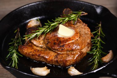 Kemiğin üzerinde domuz pirzolası bir parça tereyağında sarımsak ve biberiyeyle kızartma tavasında. 