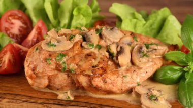 Mantar soslu tavuk göğsü ve ahşap tabakta sebzeler. Soldan sağa dairesel hareket.