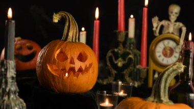 Cadılar Bayramı. Masada yanan mumlar arasında parlayan balkabağı Jack o fener, yatay, yavaş çekim video, sağdan sola hareket