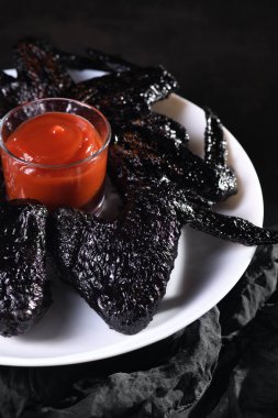 Yarasa kanatları. Tatlı ve ekşi sosta mürekkepbalığıyla pişirilmiş, tabakta ketçapla servis edilmiş. Cadılar Bayramı partisi için orijinal bir fikir.