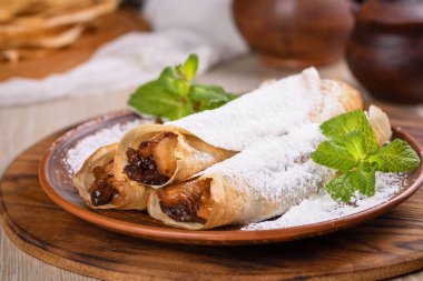 Ev yapımı ince krepler. Elmalar tereyağlı karamel sosunda, kuru üzüm ve tarçınla pişiriliyor ve ince bir krebin içine dolduruluyor. Pudra şekeri ve naneli garnitür. Kaba bir yemek..