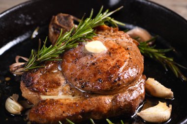 Kemiğin üzerinde domuz pirzolası bir parça tereyağında sarımsak ve biberiyeyle kızartma tavasında. 