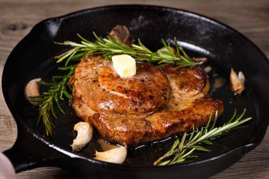 Kemiğin üzerinde domuz pirzolası bir parça tereyağında sarımsak ve biberiyeyle kızartma tavasında. 