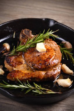 Kemiğin üzerinde domuz pirzolası bir parça tereyağında sarımsak ve biberiyeyle kızartma tavasında. 