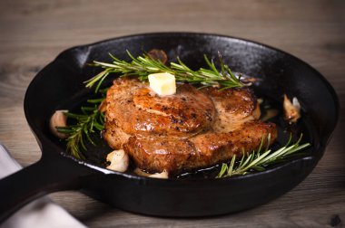 Kemiğin üzerinde domuz pirzolası bir parça tereyağında sarımsak ve biberiyeyle kızartma tavasında. 