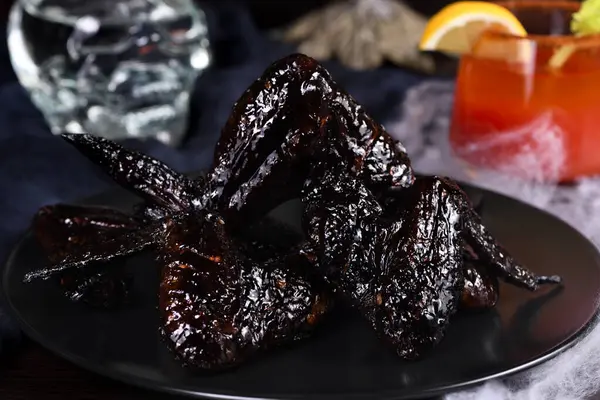 Yarasa kanatları. Tatlı ve ekşi sosta mürekkepbalığıyla pişirilmiş, tabakta ketçapla servis edilmiş. Cadılar Bayramı partisi için orijinal bir fikir.