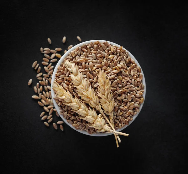 ボウルと全体の小麦の耳 クローズアップで小麦の穀物 黒の背景にファロ小麦のヒープ トップビュー 食品業界のパン成分のためのグルテンタンパク質と穀物種子 ストックフォト