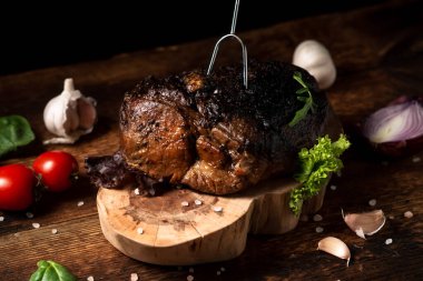 Ahşap tezgahta pişmiş bir parça et ve çiğ sebze. Baharatlı fırında pişirilmiş domuz ya da sığır eti..
