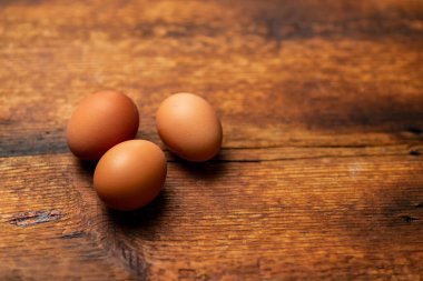 three chicken whole eggs on a wooden surface. Side view.