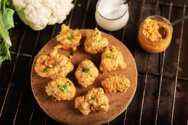 Pieces of flour-fried cauliflower with vegan sauces on a plate on a dark background. Cauliflower wings food.