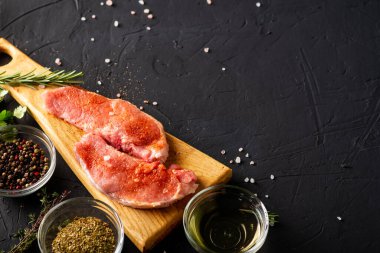 Kesme tahtasında çiğ et. Karanlık arka plan. Domuz eti pişirme hazırlığı. Yakınlarda çeşitli baharatlar ve baharatlar var..
