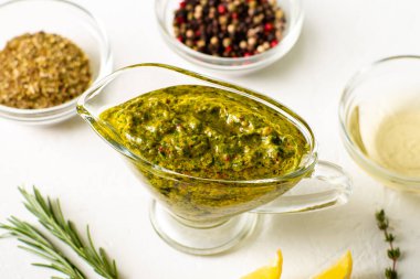 Beyaz arka planda soslu Chimichurri sosu. Yakınlarda çeşitli baharatlar var. Arjantin vejetaryen sosu zeytinyağı, kekik, maydanoz.