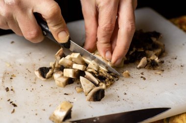 Kesme tahtasında dilimlenmiş şampiyon mantarları. Kadınların elleri bıçakla mantar kesiyor..