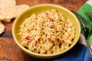 couscous, spices and tomato tabbouleh salad with rice bread in a yellow plate on a wooden background. Traditional oriental salad, appetizer.