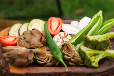 Artichokes, broccoli, onions, tomatoes and various vegetables on a wooden tray. Vegan healthy food, diet concept. Preparing to cook grilled vegetables.