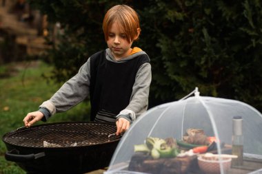The boy prepares a round grill for grilling.