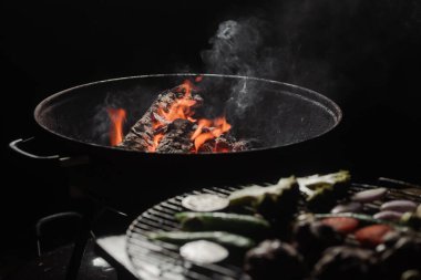 Firewood burns in a round barbecue at night. Dark background. Preparing to cook food on the grill.