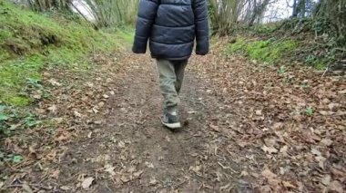 The boy slowly walks along the forest path, rear view on his feet. Forest area in autumn or spring.