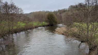 Forest meandering river flows. Rural natural area with hills and forests.