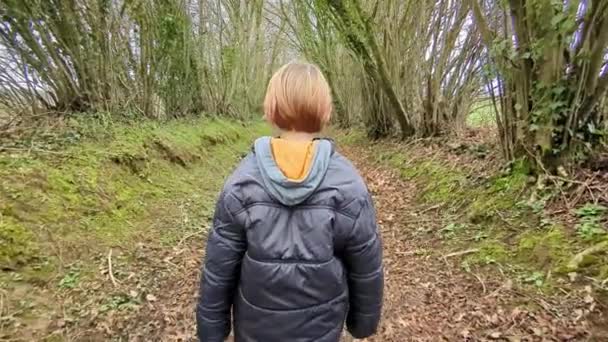 少年は森の道 リアビューに沿って歩いている 長い黄色い髪の男の子 春の森林面積 — ストック動画