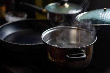 A pot of boiling water on a kitchen stove. Kitchen utensils are nearby.